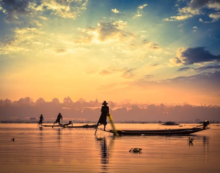 Myanmar travel attraction landmark - traditional Burmese fishermen sihouettes at Inle lake on sunset, Myanmar famous for their distinctive one legged rowing style