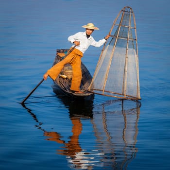 Myanmar travel attraction landmark - Traditional Burmese fisherman with fishing net at Inle lake in Myanmar famous for their distinctive one legged rowing style