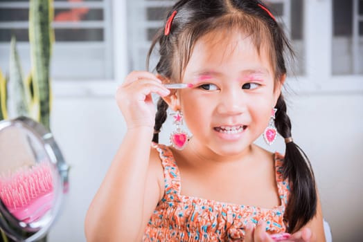 Happy kid is beautiful make up with cosmetics toy, Asian adorable funny little girl making makeup her face she applying carborundum eyeliner to eyelid, Learning activity to be woman at house