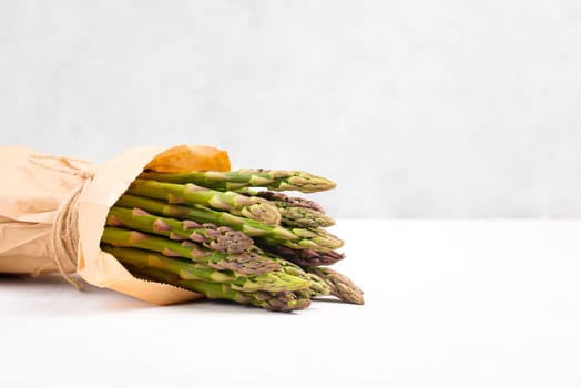 Fresh green bundle of asparagus on a white textured table, vegetables in spring, gourmet cuisine food, cooking a vegan meal