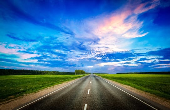 Travel concept background - road and stormy dramatic sky on sunset