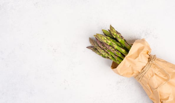 Fresh green bundle of asparagus on a white textured table, vegetables in spring, gourmet cuisine food, cooking a vegan meal