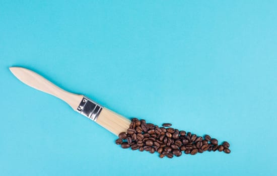 Painting with a brush a line with roasted coffee beans, blue background with copy space, having a hot drink for breakfast, taking a break
