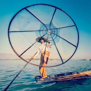 Vintage retro effect filtered hipster style image of Myanmar travel attraction. Traditional Burmese fisherman with fishing net at Inle lake famous for their distinctive one legged rowing style