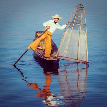 Vintage retro effect filtered hipster style image of Myanmar travel attraction. Traditional Burmese fisherman with fishing net at Inle lake famous for their distinctive one legged rowing style