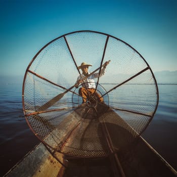 Myanmar travel attraction - Traditional Burmese fisherman with fishing net at Inle lake in Myanmar, view from boat. Vintage filtered retro effect hipster style image