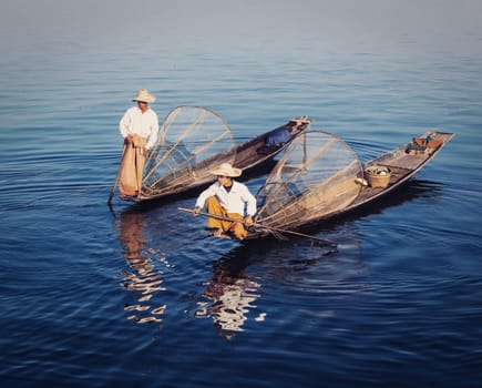 Myanmar travel attraction - Traditional Burmese fishermen with fishing net at Inle lake in Myanmar famous for their distinctive one legged rowing style. Vintage filtered retro effect hipster style image