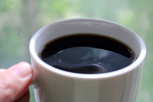 White mug with black coffee in hand close-up..