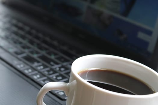 A white mug with black coffee close-up against the background of a black laptop. Business concept..