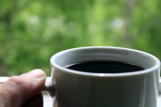 White mug with black coffee close-up on a natural green background..