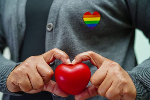 Asian woman holding red hert with rainbow flag, LGBT symbol rights and gender equality, LGBT Pride Month in June.