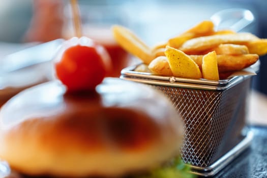Focus in the background on french fries in a mesh basket standing near a burger.