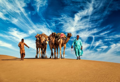Rajasthan travel background - two Indian cameleers (camel drivers) with camels in dunes of Thar desert. Jaisalmer, Rajasthan, India