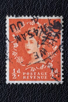 Potsdam, Germany - APR 26, 2022. A old of Great Britain (United Kingdom) issued stamp with portrait of Queen Elizabeth II with postmark on a black leather background. Orange. ½ d