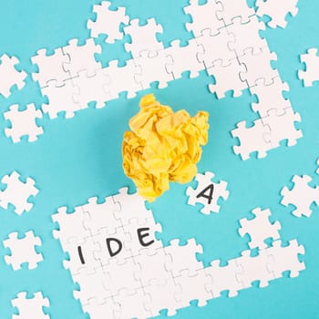 Puzzle on a blue background, yellow crumbled paper, word idea is standing on the jigsaw pieces, brainstoming concept, working as a team together