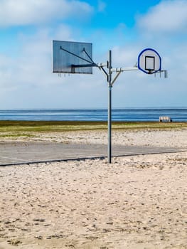 Half side view of a two-sided street basketball hoop mast on the North Sea beach in Harlesiel Ostfriesland in front of a blue sky in vertical orientation.