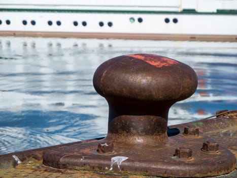Low angle closeup of a steel bollard in Carolinensiel harbor with island ferry in blurred background in daylight and sunshine.