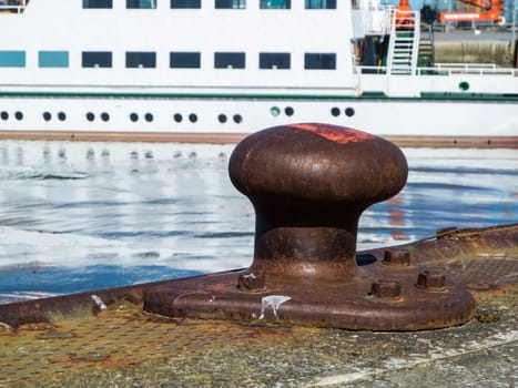 Low angle closeup of a steel bollard in Carolinensiel harbor with island ferry in blurred background in daylight and sunshine.