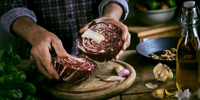 High angle of crop man in checkered shirt putting halves of red cabbage on cutting board near garlic and basil with oil and walnuts during healthy lunch preparation in rustic kitchen