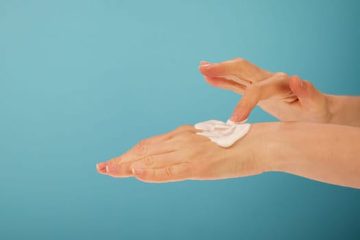 Unrecognizable female applying soft cream on hand with index finger during beauty routine against turquoise background