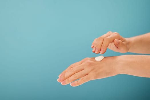 Anonymous woman ready to spread natural cream on back of hand with clean skin against turquoise background
