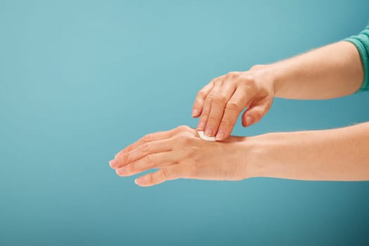 Crop female applying moisturizing cream on hands during spa session against turquoise background