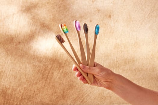 Anonymous female with set of assorted multicolored natural bamboo toothbrushes for eco friendly daily oral care against beige background