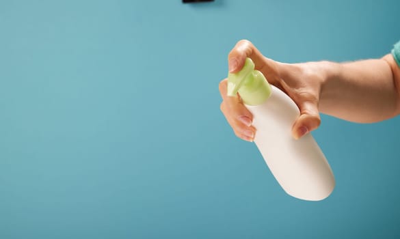 Unrecognizable woman pushing dispenser to apply soap from bottle during hygienic routine against turquoise background.