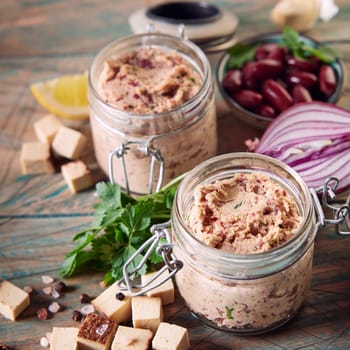 From above of delicious healthy vegetarian pate with red beans and herbs in glass jars served on wooden table near cubed cheese and halved onion in kitchen
