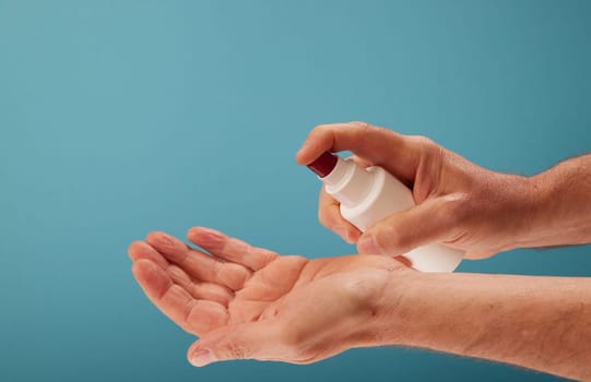 Anonymous male spraying sanitizer from bottle on hand during hygienic routine against turquoise background