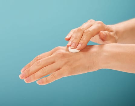 Anonymous woman rubbing drop of moisturizing cream into delicate skin of hand against turquoise background