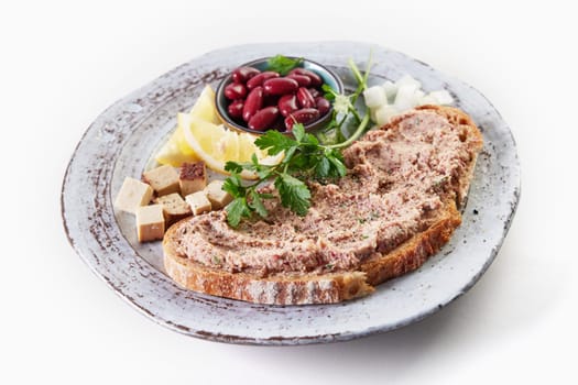 From above of appetizing toast with homemade vegetarian liverwurst pate served on plate with bowl of red beans cubed cheese and lemon on white background