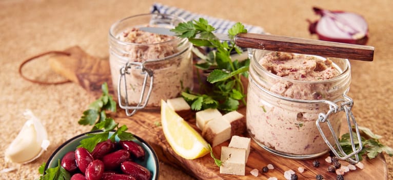 From above of delicious vegetarian liverwurst in pint jars with lemon slices and fresh parsley served on wooden board near bowl of marinated red beans in kitchen