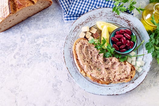Top view of yummy bruschetta with vegetarian liverwurst pate served on plate with red beans cubed cheese and sliced lemons on table near carafe of olive oil and bread