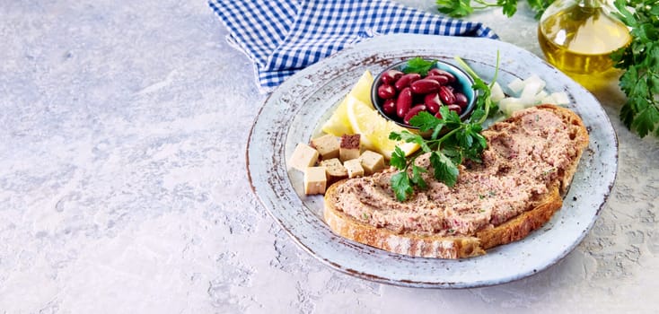 From above of yummy crunchy bread with homemade vegetarian liverwurst pate served on plate with bowl of kidney beans sliced lemons and cheese on table in kitchen
