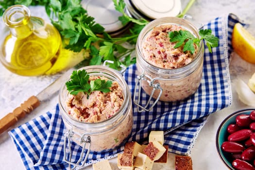 From above of delicious vegetarian liverwurst pate with red bean and onion in glass jars placed on checkered napkin near cubed cheese carafe of olive oil and parsley in kitchen