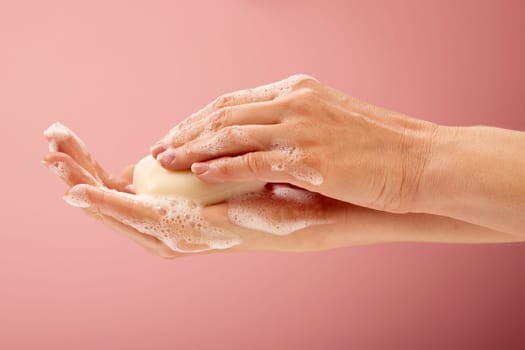 White soap in the hands of a natural woman on pink surface.