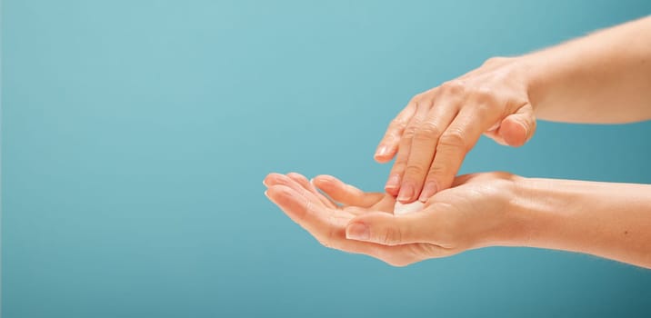Crop female taking moisturizing cream from open palm during skin care procedure against turquoise background