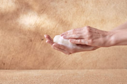 Woman hands touching foamy soap on beige background for spa advertising