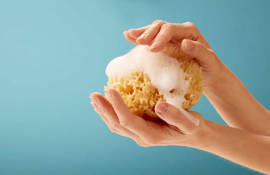 From above of crop anonymous female touching soft yellow sea sponge against blue background