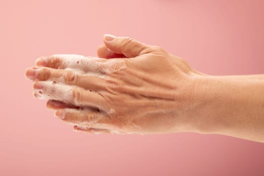 female washing her hands on a pink surface with foam on the fingers and arms.
