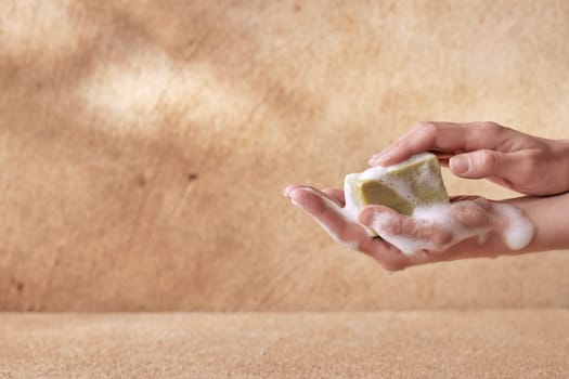 Sensitive hands of female holding soap with foam on brown background for skin and health care conceptual designs with copyspace.