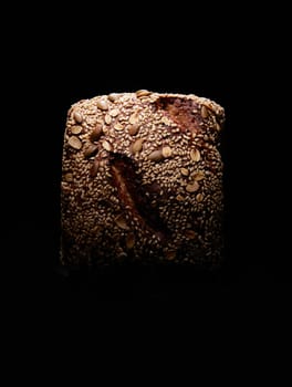 Top view of square shaped baked loaf of farmers bread with grains placed on black background in studio with dim light
