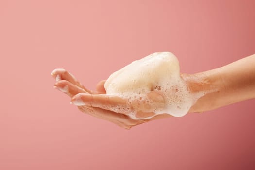Hand with soap and foam on bright pink background for healthcare concepts.