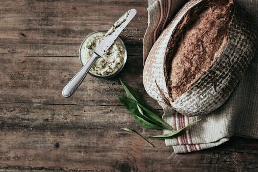 Top view of freshly baked loaf of bread placed on wooden table with jar of lard and towel in light kitchen