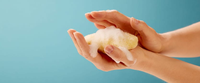 Crop hand of anonymous female applying moisturizing sponge on blue background in studio