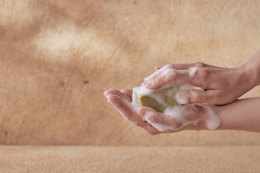 Crop female hand holding olive soap with foam with copyspace on brown background for healthcare and washing concepts
