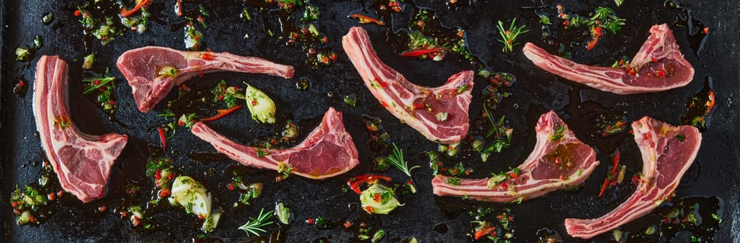 Top view panorama of fresh raw lamb chops and chopped green with chili pepper on black background in light kitchen