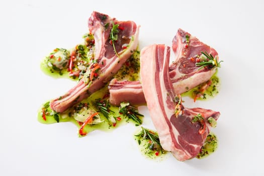 From above of uncooked lamb chops placed on white background with oil and chopped greens with garlic in light kitchen