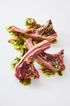 From above of raw fresh lamb chops covered with oil and chopped greens served on white background in light kitchen